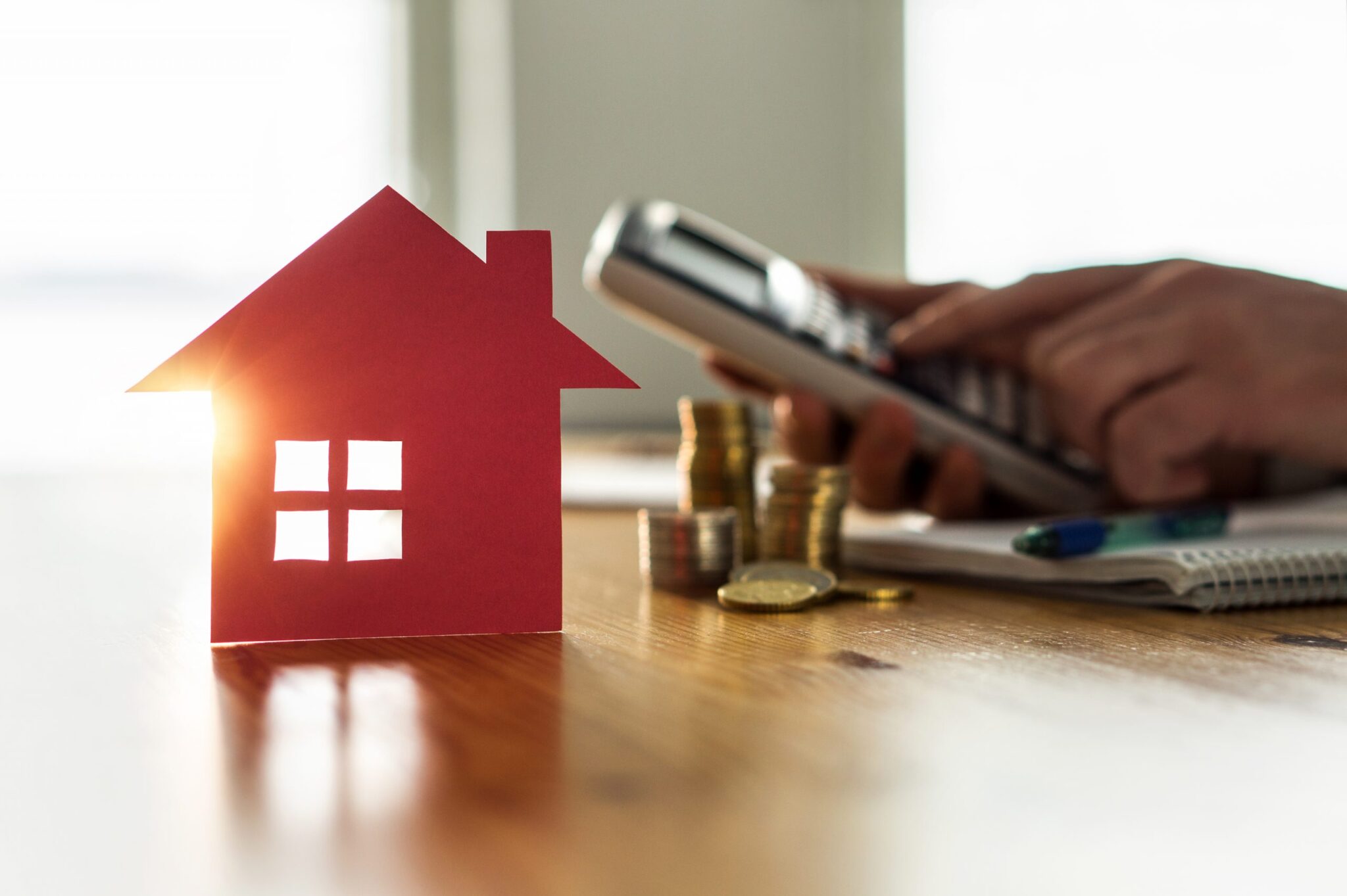 an image of a person calculating something next to a pile of coins and a cutout of a house to denote a story about UK house prices