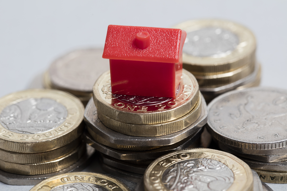 a toy house on top of coin stacks to denote mortgage payments