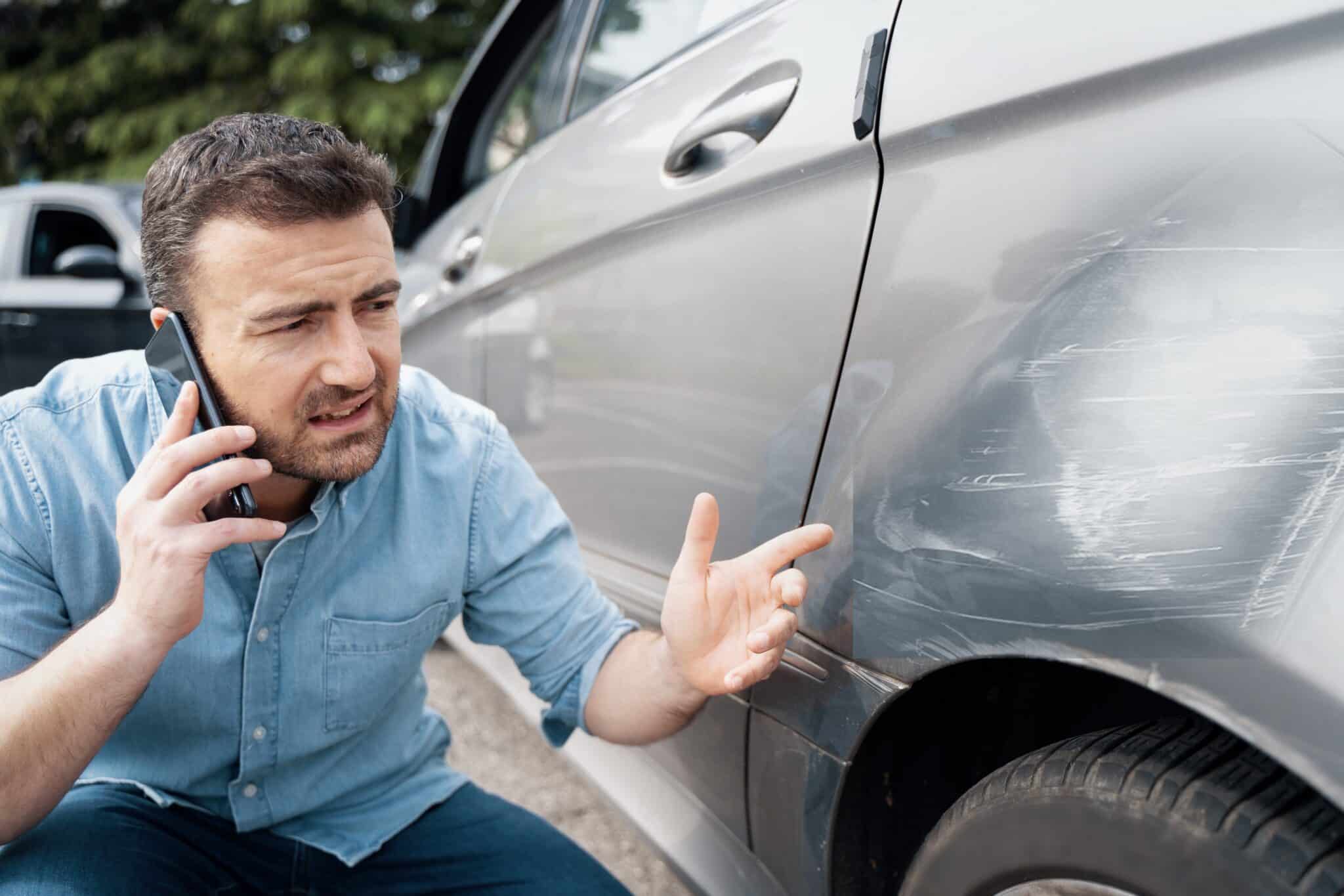 a photo of a man making a call about the damage of a car as hire car damage for drivers goes unrecorded