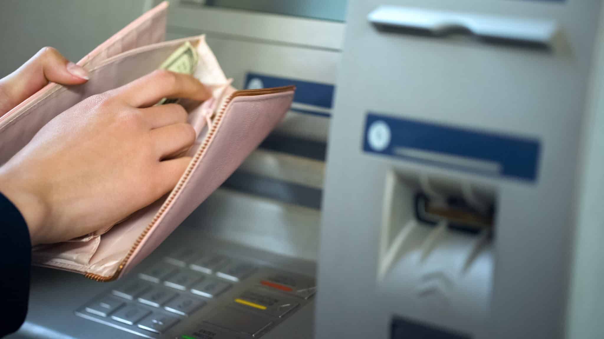 image of someone putting cash into their wallet at and ATM machine to denote credit card withdrawals abroad