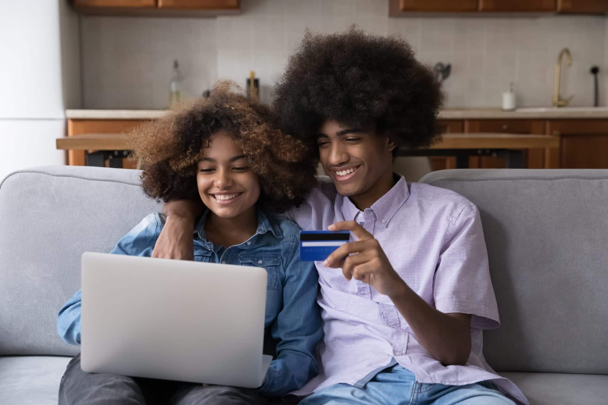 two Gen Z adults on a laptop smiling with a card to denote UK Savings week 2024