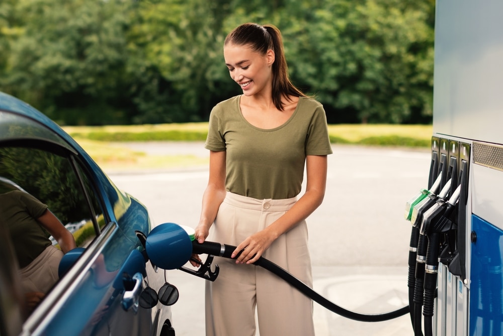 a happy woman filling up her car as petrol prices drop