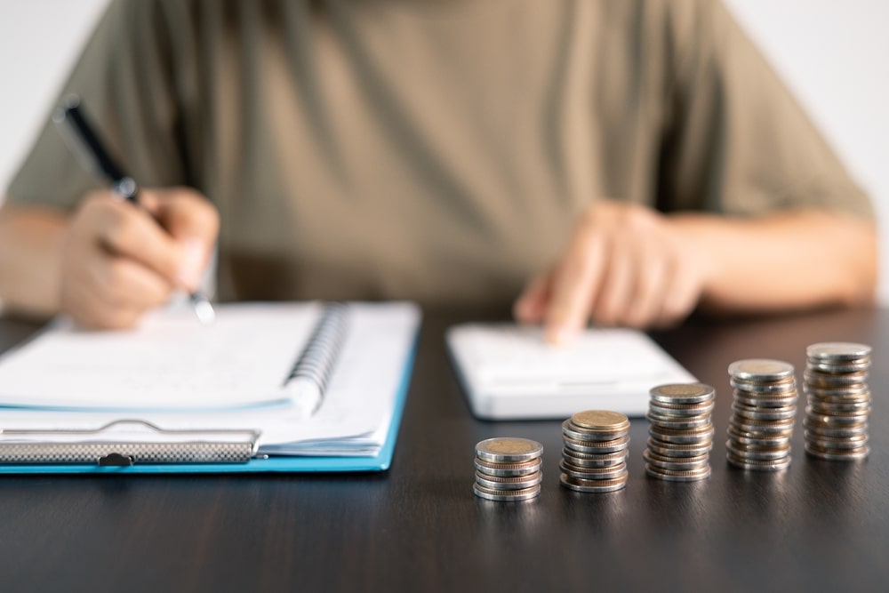 An image of someone signing a contract with a stack of coins rising