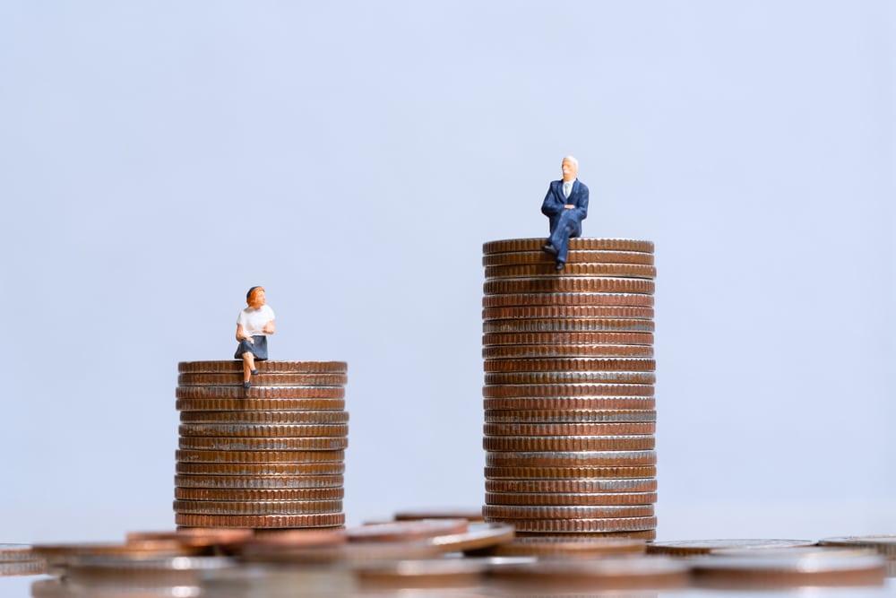 Two stack of coins with a woman on the shorter stack and man on the taller one to denote the gender pensions gap