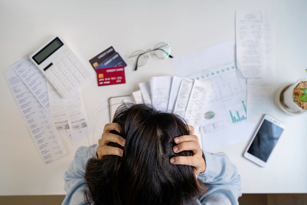 A woman with head in her hands with bills to denote a blog on financial worries