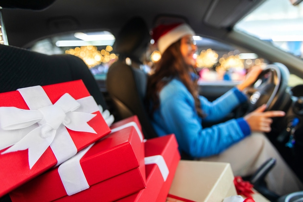 A stack of presents in the foreground with a driver next to them to denote petrol prices for families driving home for christmas