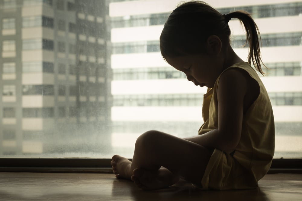 Silhouette of a sad child in a window to denote a story on child poverty