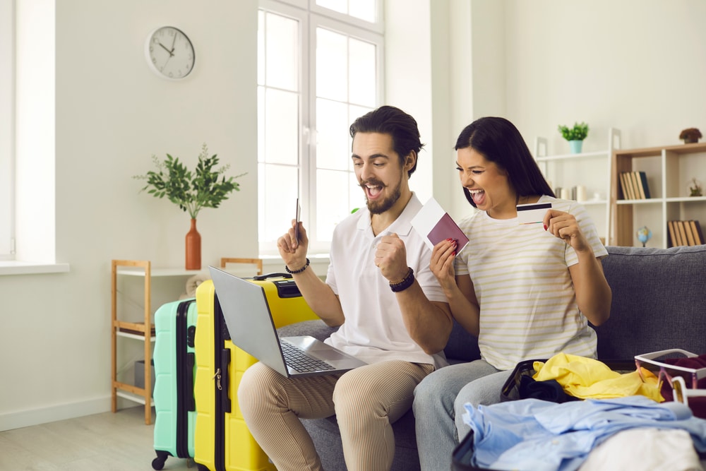 A couple celebrating booking a cheap flight on laptop to denote when to book flights for the cheapest prices