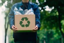 Man holding recycling box with plastic bottles to denote a story on how to earn cash for plastic recycling